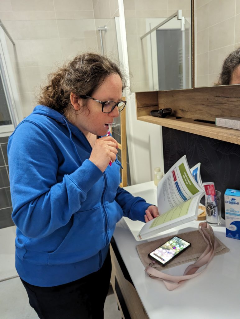 Fille en train de se brosser les dents, un livre à la main.